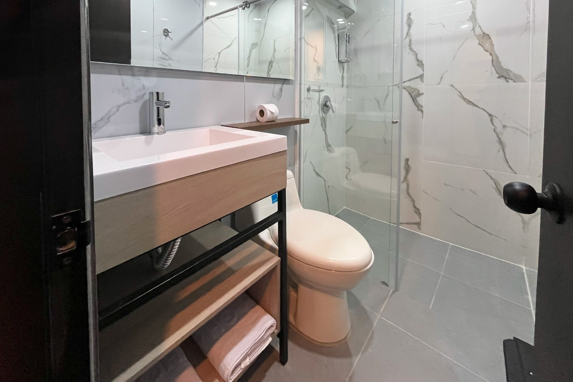 A modern bathroom with a marble backsplash, a sink with a mirror, a toilet, and a shower area.