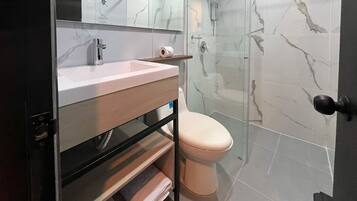 A modern bathroom with a marble backsplash, a sink with a mirror, a toilet, and a shower area.