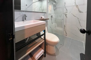 Une salle de bain moderne avec un pare-baignoire en marbre, un lavabo avec un miroir, des toilettes et un espace douche.