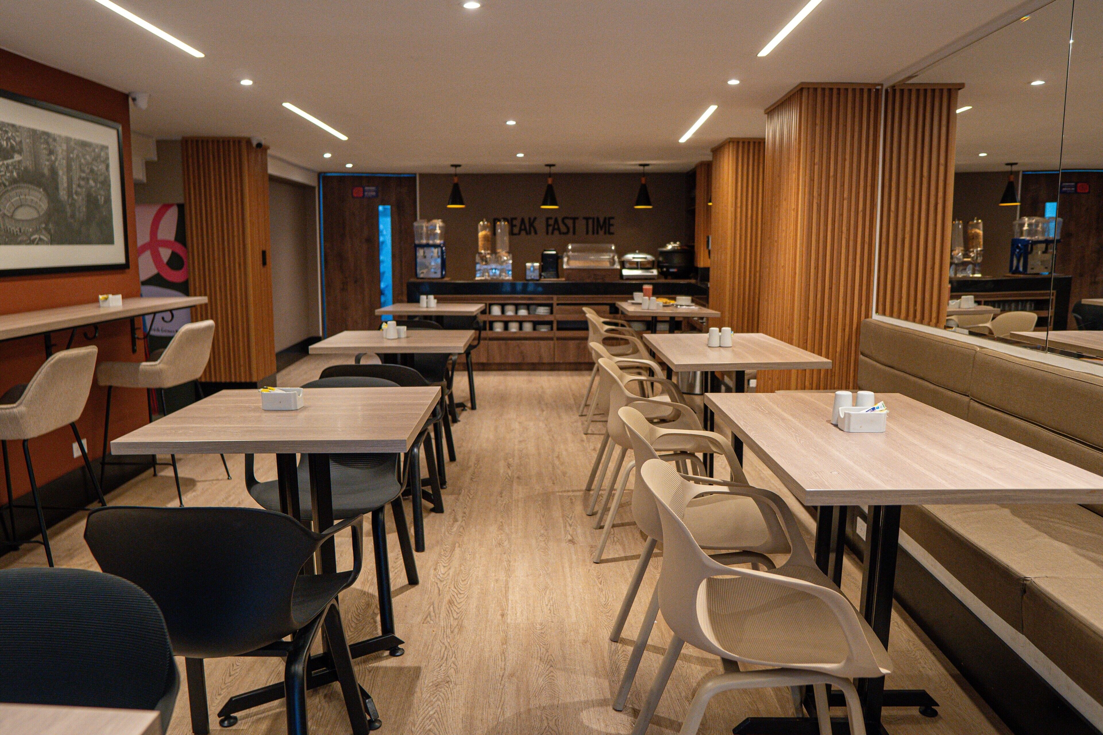 Un restaurant moderne doté de nombreuses tables et chaises, d’un bar et d’un mur orné d’une horloge et d’une enseigne.