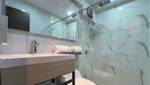 Une salle de bain moderne avec une douche à parois de verre, des toilettes blanches et un meuble-lavabo avec un pare-éclaboussures en marbre.
