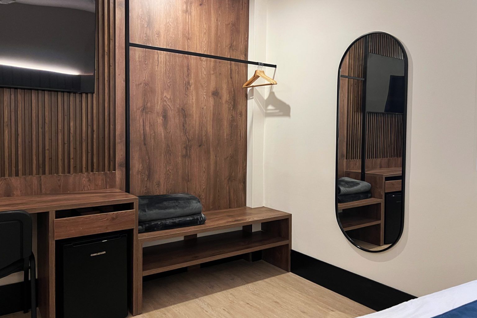 A modern bedroom with a wooden vanity, a bench, a mirror, and a small black appliance.