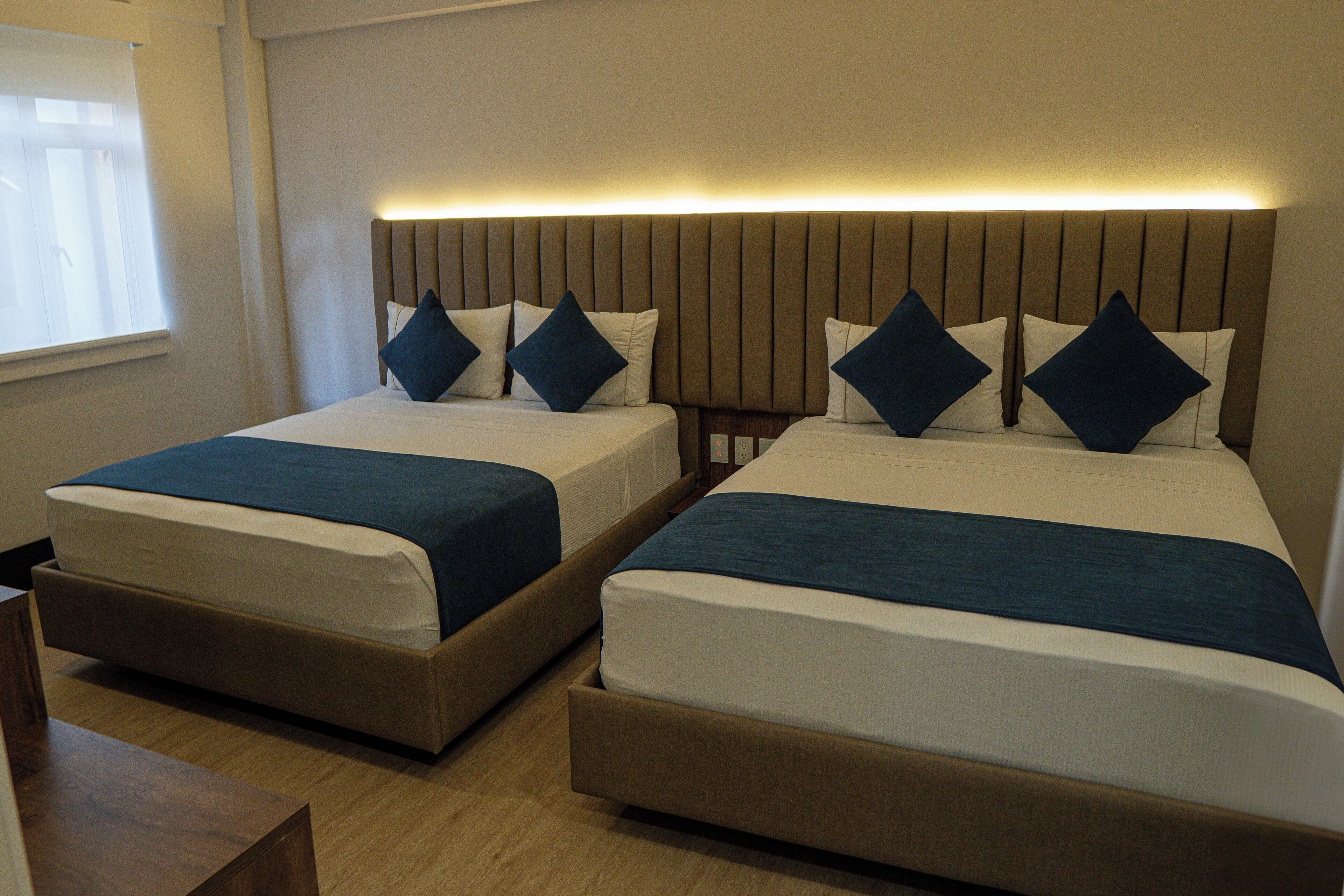 Une chambre d’hôtel avec deux lits simples, une tête de lit en bois et une table de chevet.