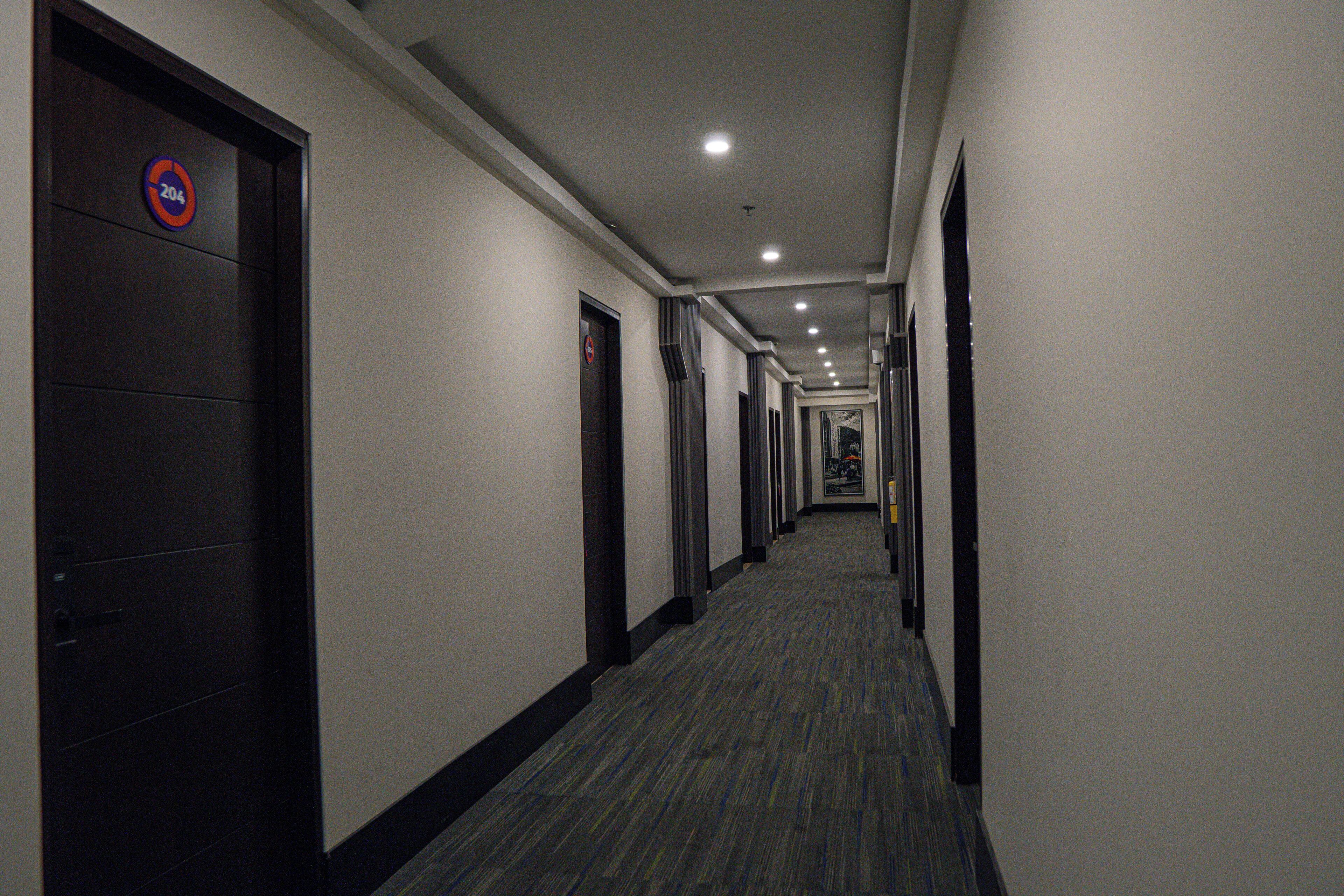 A hotel hallway with doors, a carpeted floor, and a ceiling with recessed lighting.