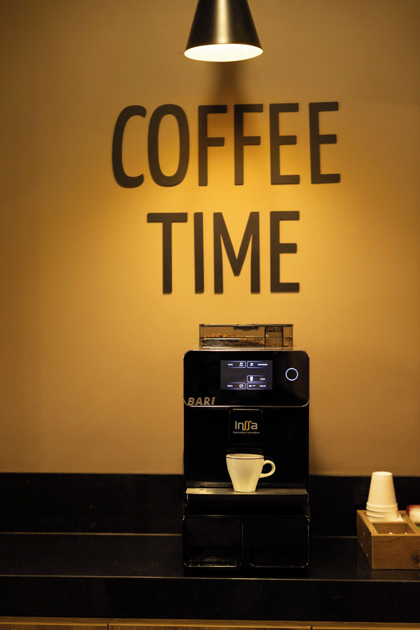 Una cafetera sobre una encimera con una taza y un portavasos para café, y un cartel que dice "COFFEE TIME".
