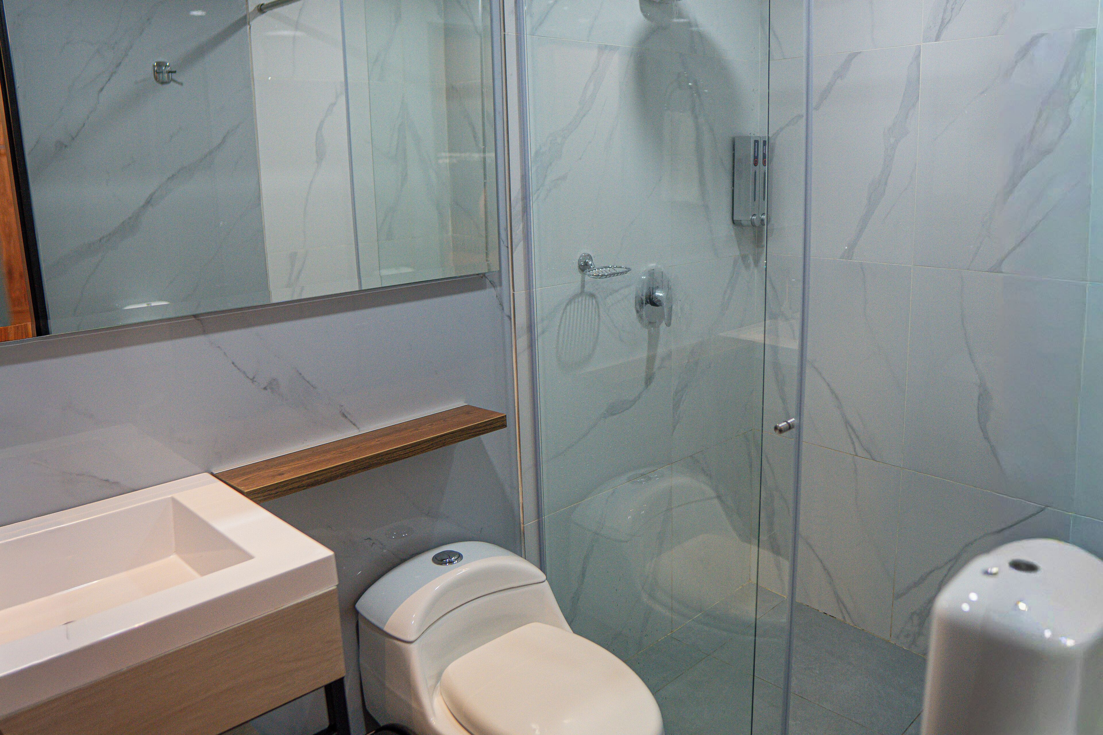 Un bany modern amb dutxa tancada amb vidre, un vàter i un lavabo amb taulell de fusta.