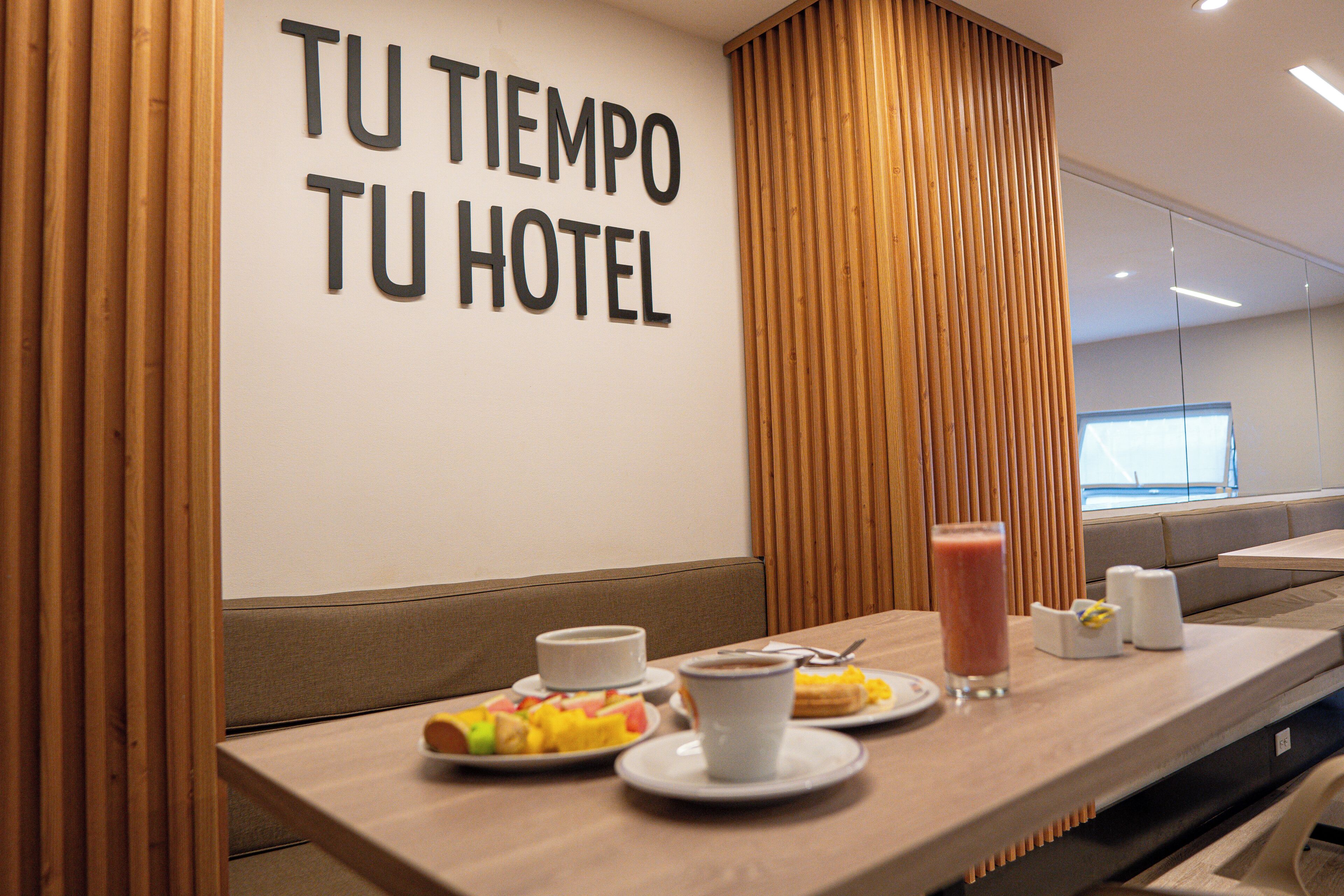 Et hotelreception med et skilt der siger 'TU TIEMPO TU HOTEL' og et morgenmålsbord med tallerkener, kopper og et glas juice.