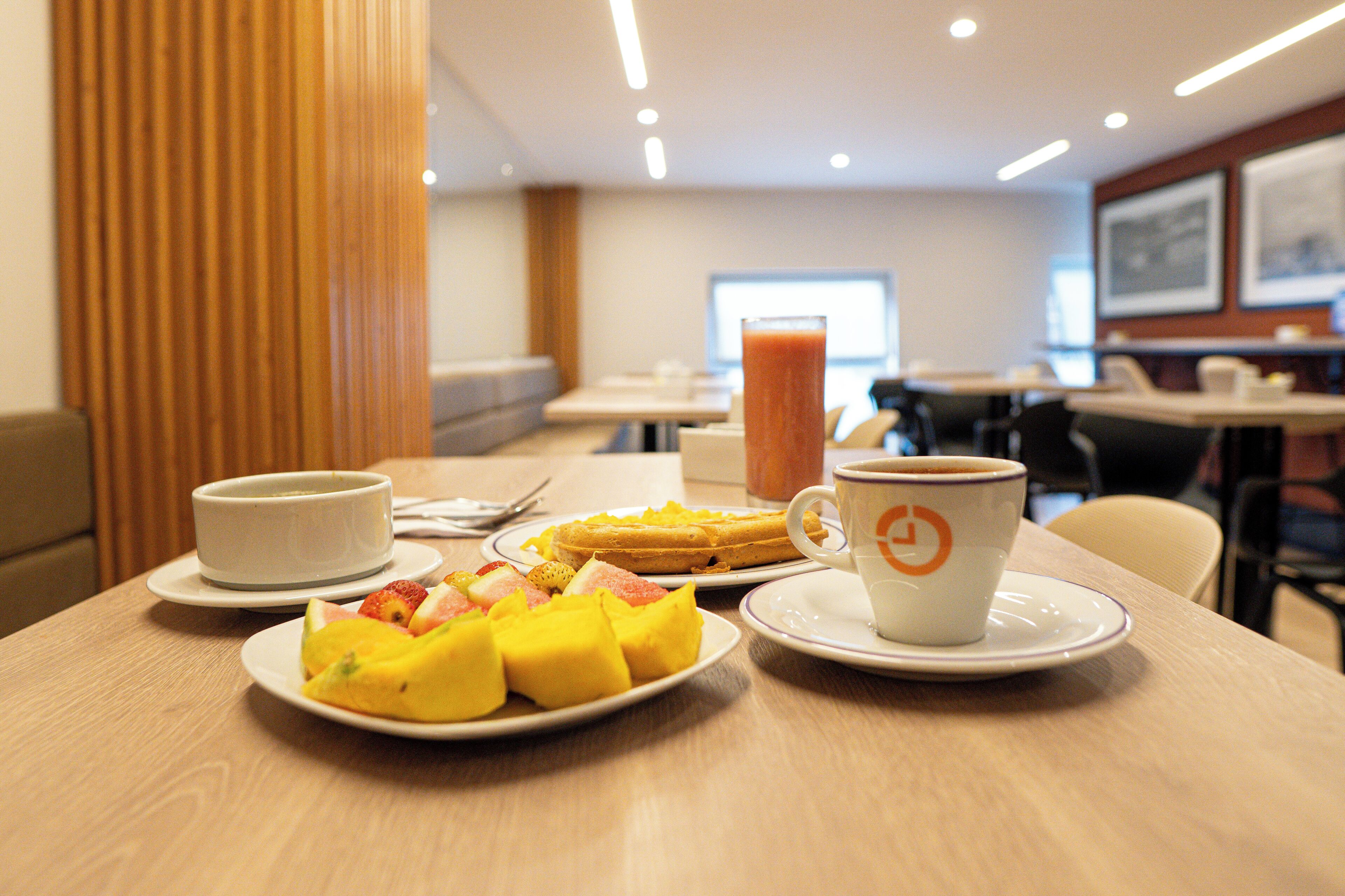 A breakfast setting with a plate of fruit, a cup of coffee, and a glass of orange juice on a table.