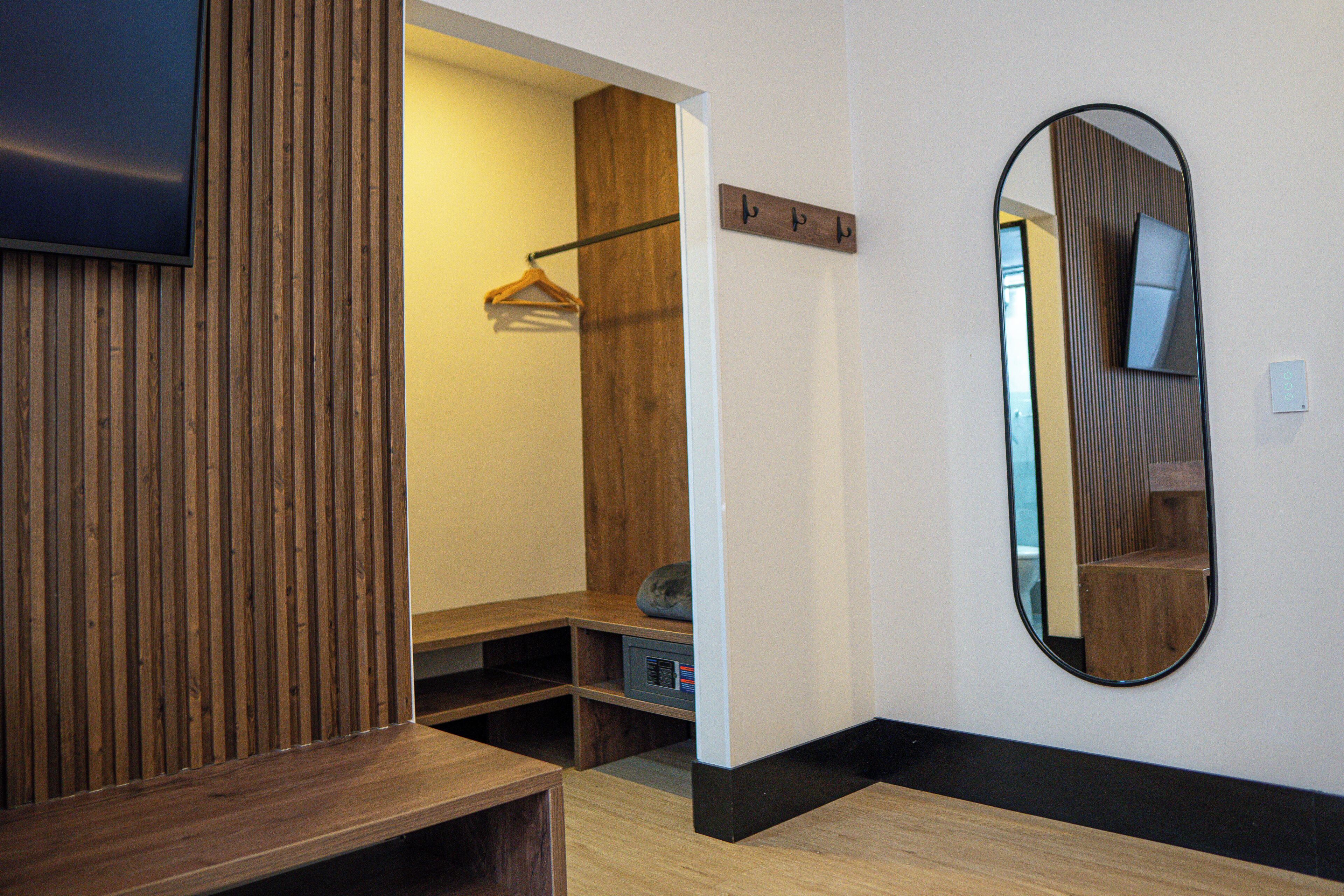 A hotel room with a wooden panel wall, a mirror, a coat rack, and a small seating area.