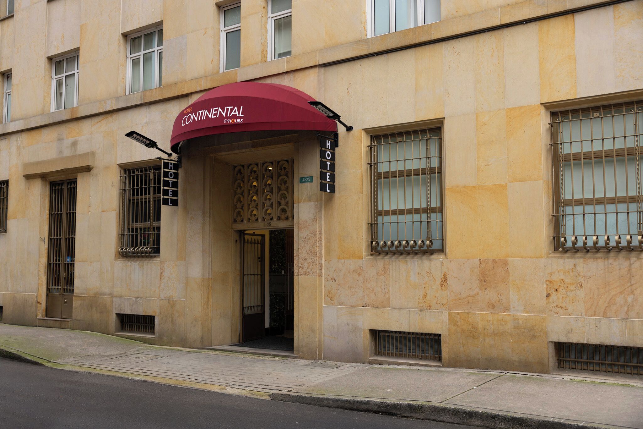 A hotel entrance with a maroon awning, a sign indicating the name 'Continental Hotel', and a number '4-25' on the door.