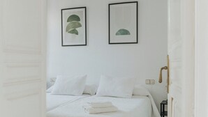 Un dormitorio minimalista con una cama, dos obras de arte enmarcadas y un ventilador de techo.