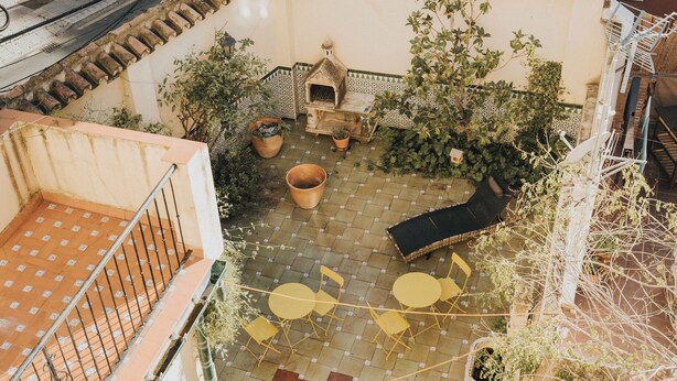 Un patio con suelo de baldosas, un pequeño horno de ladrillo, sillas amarillas y plantas en macetas.