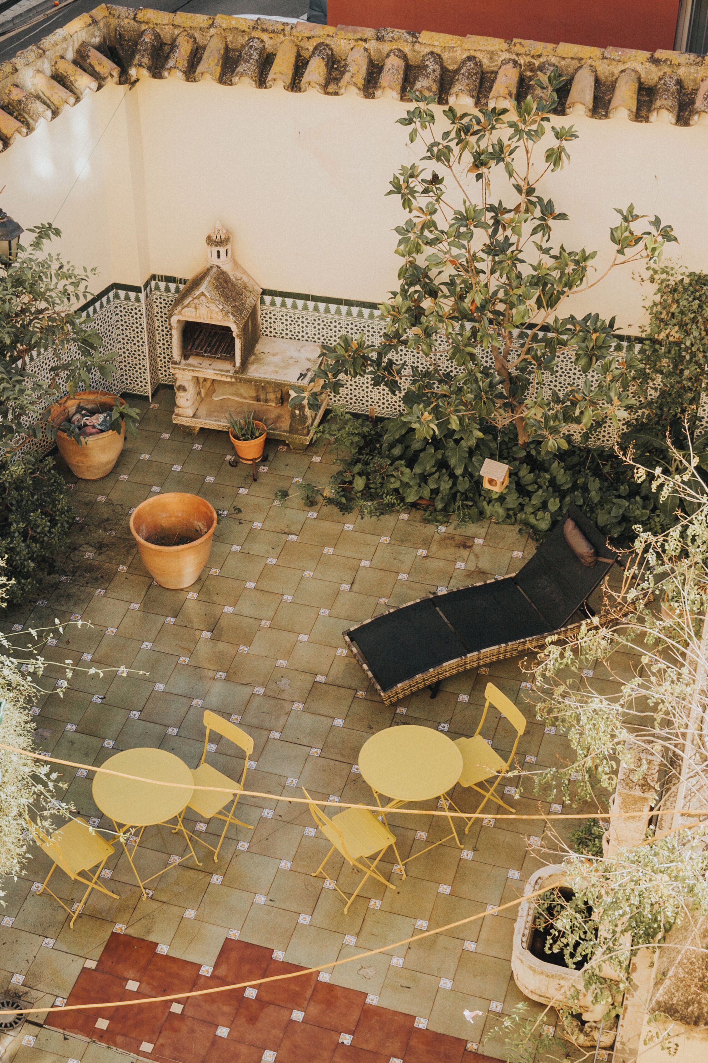 An outdoor patio with a sun lounger, yellow chairs, and potted plants.