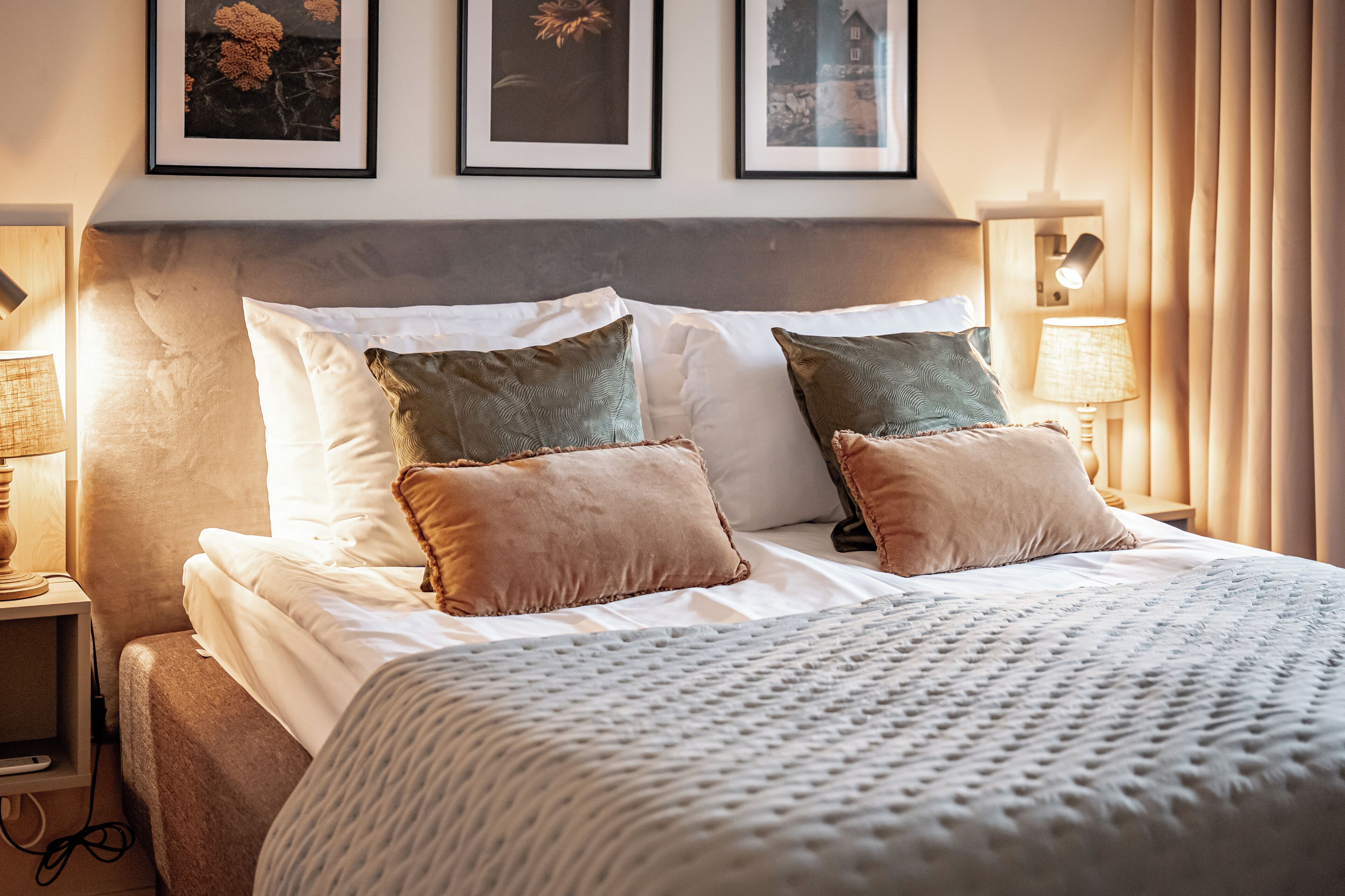 A neatly made bed with white and brown bedding, a headboard, and two wall-mounted lamps.
