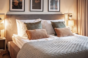A neatly made bed with white and brown bedding, a headboard, and two wall-mounted lamps.