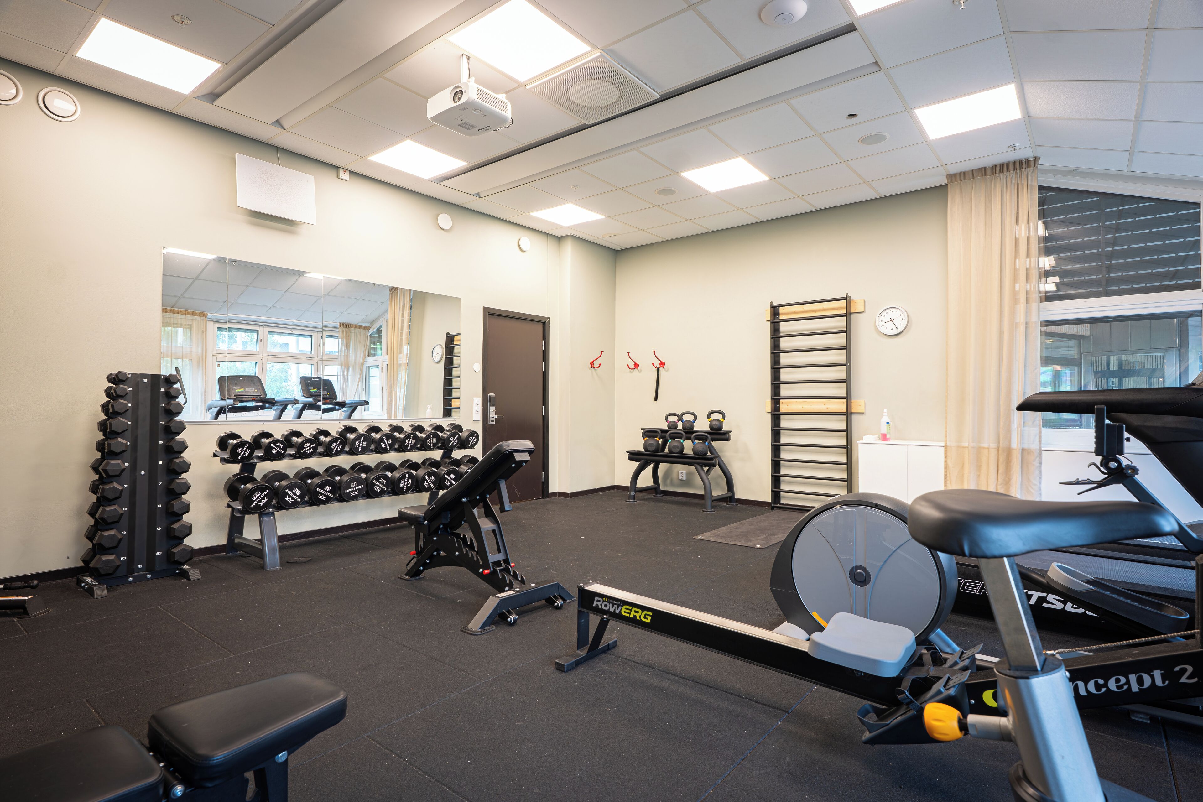 Un gimnasio con equipo de ejercicio, un espejo y una ventana con cortinas.