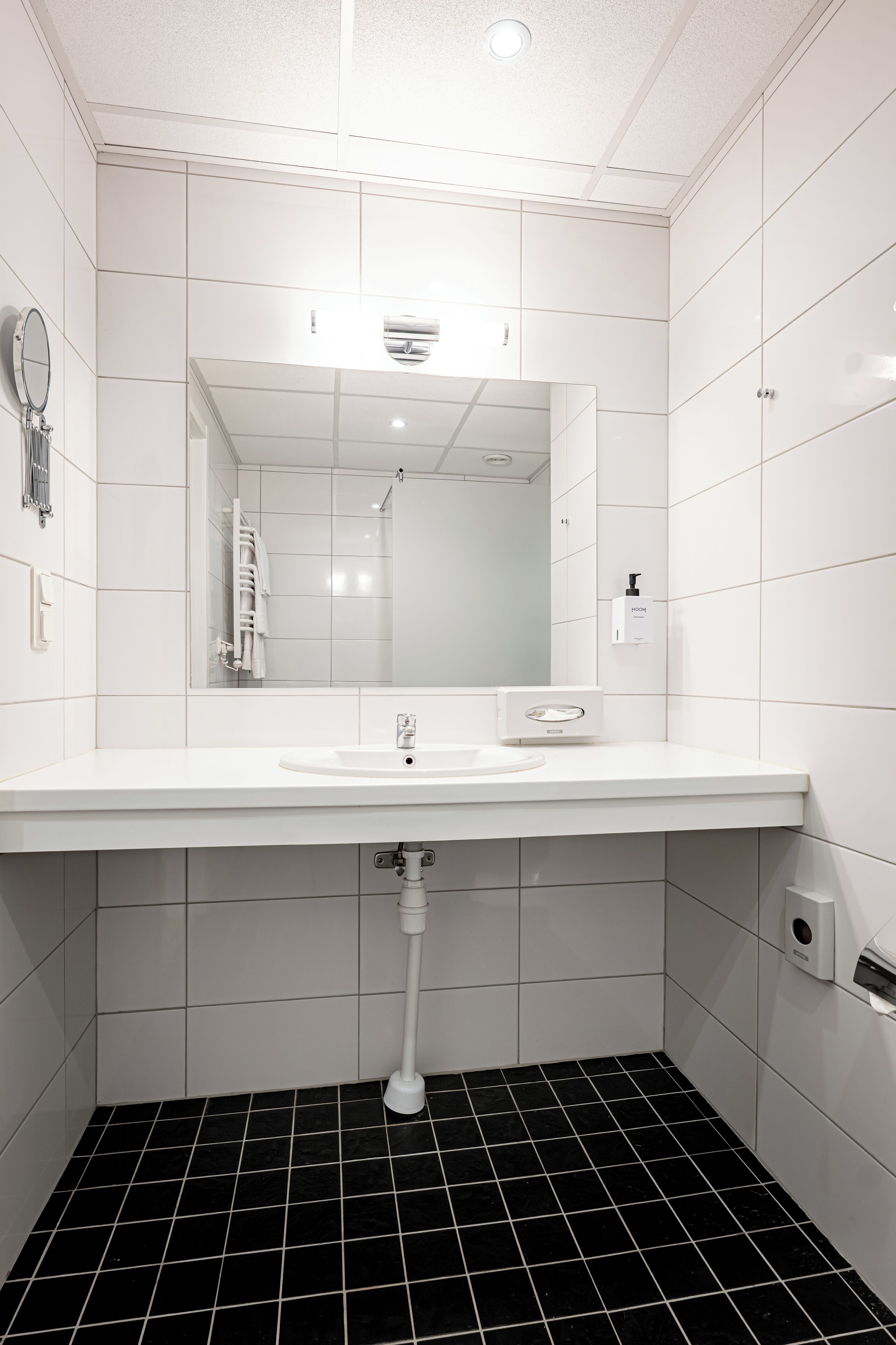 A modern bathroom with a white sink, a mirror, and a black-tiled floor.