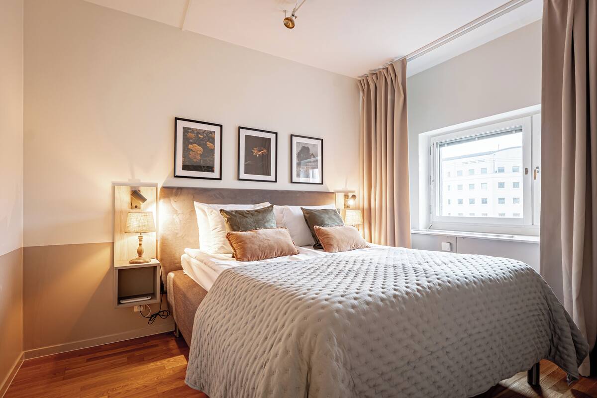 Ein ordentlich eingerichtetes Schlafzimmer mit einem großen Bett, Nachttischlampen und gerahmten Bildern an der Wand.