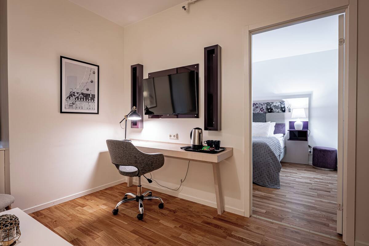 Ein modernes Schlafzimmer mit Holzboden, einem Schreibtisch mit Stuhl, einem Bett und einem an der Wand befestigten Fernseher.