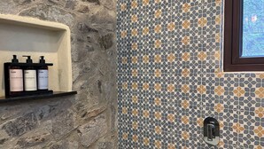 Un baño con pared de piedra, pared de ducha azulejada y estante con tres botellas etiquetadas "O4N acondicionador champú gel de baño".