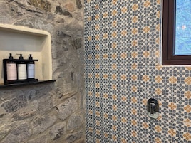 Un baño con pared de piedra, pared de ducha azulejada y estante con tres botellas etiquetadas "O4N acondicionador champú gel de baño".