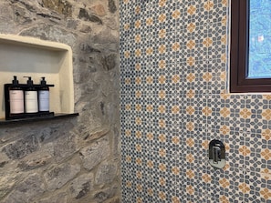 Un baño con pared de piedra, pared de ducha azulejada y estante con tres botellas etiquetadas "O4N acondicionador champú gel de baño".