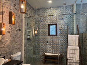 A bathroom with a stone wall, a glass shower enclosure, a wooden bench, and a towel rack. - Castello di Carlo - Suite Carlo I (Tetlatlahuca)