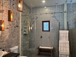 Un baño con pared de piedra, cabina de ducha de vidrio, banco de madera y perchero.