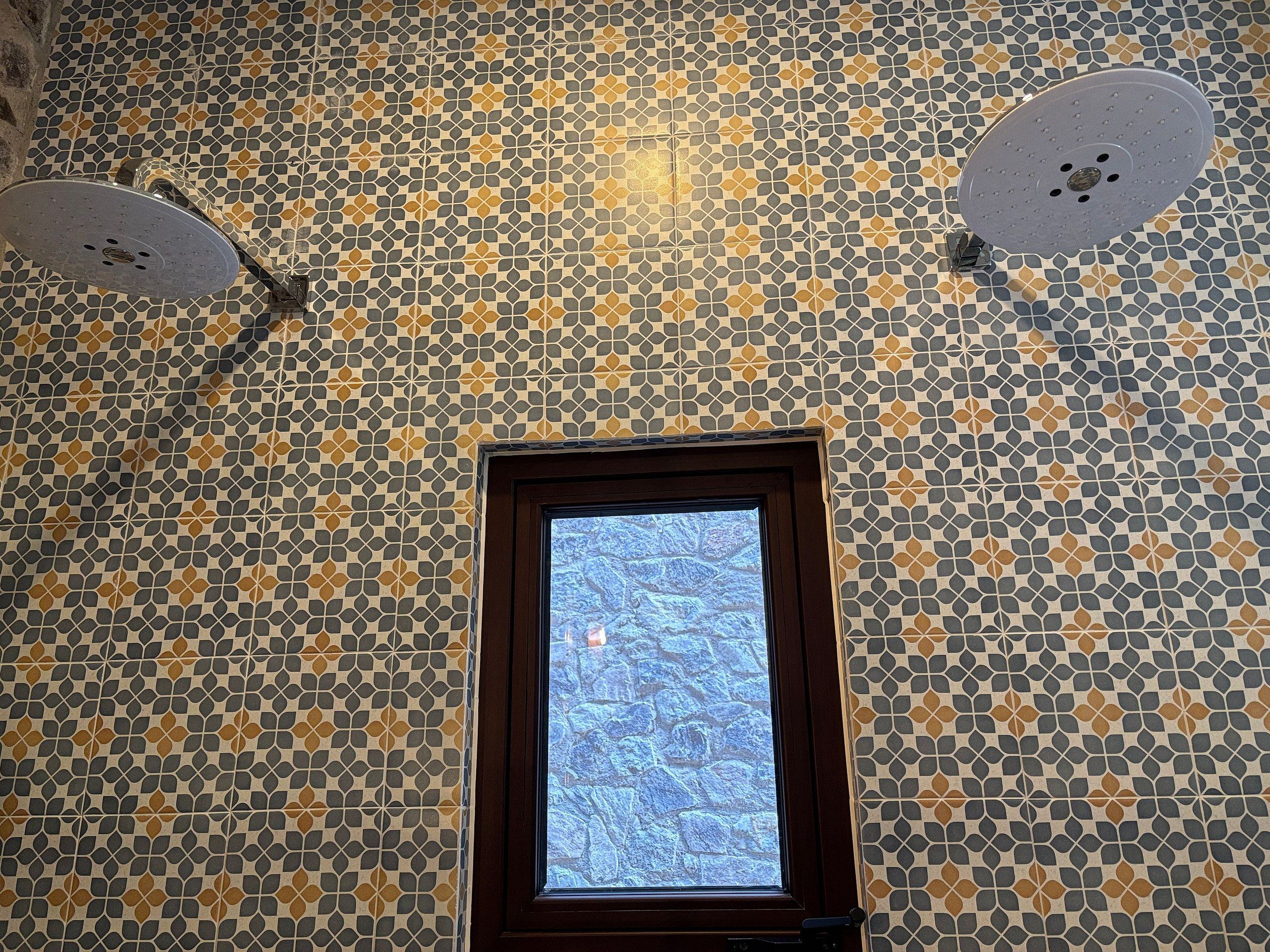 Una habitación con pared de baldosas estampadas, una ventana y un ventilador de techo.