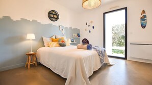 A bedroom with a bed, a nightstand, a lamp, a window, and a surfboard decoration. - Modern villa with pool in the heart of Provence, 30 minutes from the beaches (Carnoules)