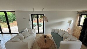 A modern living room with two white sofas, a round wooden coffee table, and a large sliding glass door leading to an outdoor area. - Superb barn in the Dordogne, in the heart of Trémolat (Trémolat)