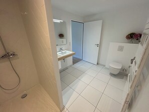 Bathroom features a shower area, sink, and toilet, set against a backdrop of large white tiles.
