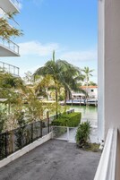 A balcony with a view of a marina, palm trees, and a building with a white facade.
