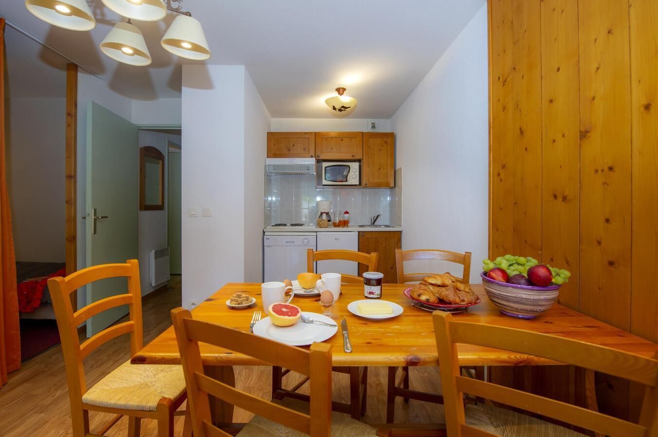 Une cuisine compacte avec des meubles en bois et un four à micro-ondes. Une table à manger, entourée de chaises, est dressée pour le petit-déjeuner.