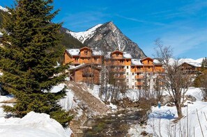 Un refugio de montaña con varias construcciones de madera, un río y paisajes nevados.