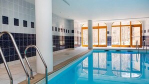 En inomhuspool med väggar av genomskinligt glas, ett kaklat golv och metallräcken.