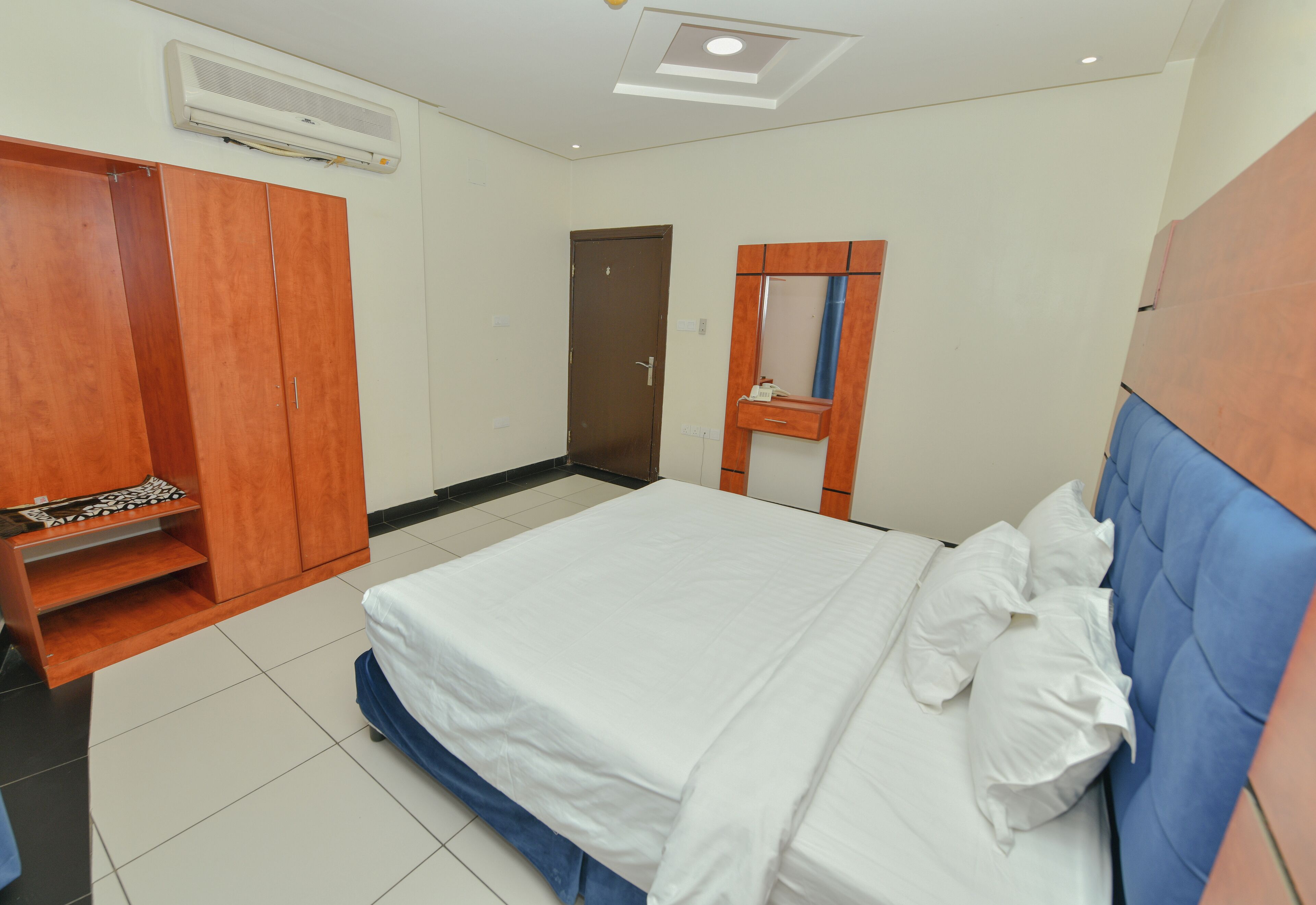 A bedroom with a bed, a wardrobe, a mirror, and an air conditioning unit.