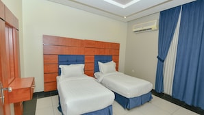 A hotel room with two single beds, a wooden headboard, a blue curtain, and an air conditioning unit on the wall. - Reef Al Kharj Hotel Apartments (Al Kharj)