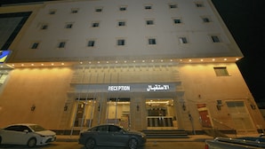 A hotel with a reception area, multiple floors, and a parking lot with cars. - Reef Al Kharj Hotel Apartments (Al Kharj)
