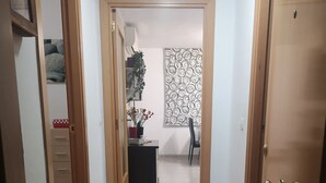 A hallway with a tiled floor, a desk with a potted plant, and a patterned wall.