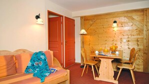 A cozy room with a wooden dining table set for two, a wooden chair, a sofa with a floral blanket, and a wooden door. - Ski-in/ski-out & foot of the slopes, fitness, swimming pool, sauna, parking, tv, 29-32m², Le Corbier (Le Corbier)