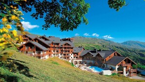 Un hotel de estilo chalete con varios balcones, piscina y montañas al fondo.