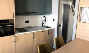 Una cocina moderna con horno integrado, un lavamanos y una zona de comedor con mesa y sillas.