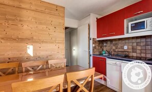 Een moderne keuken met rode kastjes, een magnetron en een vaatwasser. Er staat een houten eettafel met stoelen.