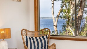A wicker chair with a striped pillow by a window overlooking a body of water and trees.