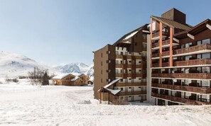 Ein mehrstöckiges Hotel mit Balkonen vor einer verschneiten Bergkulisse.