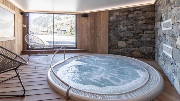 A hot tub in a wooden room with a stone wall and a view of a snowy landscape. - Wifi, 50m from ski slopes, Ground floor, view mountain/ski slopes, sauna, terrace, parking, tv (Le Grand-Bornand)