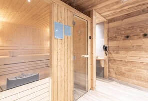 Una sauna con pareti in legno, una porta in vetro, una panca e un piccolo lavandino.