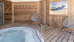A spa area with a hot tub, two metal chairs, wooden walls, and a framed picture of a snowy landscape. - Wifi, 50m from ski slopes, Ground floor, view mountain/ski slopes, sauna, terrace, parking, tv (Le Grand-Bornand)