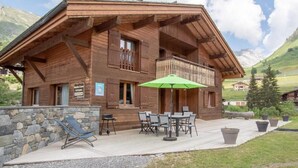 A wooden chalet with a balcony, outdoor seating, and a stone wall. - Wifi, 50m from ski slopes, Ground floor, view mountain/ski slopes, sauna, terrace, parking, tv (Le Grand-Bornand)